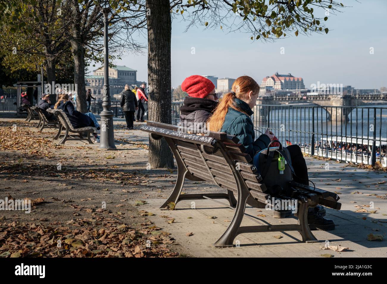 Différentes personnes assises sur un banc et regardant de la terrasse à la rivière Elbe dans la ville de Dresde. Banque D'Images