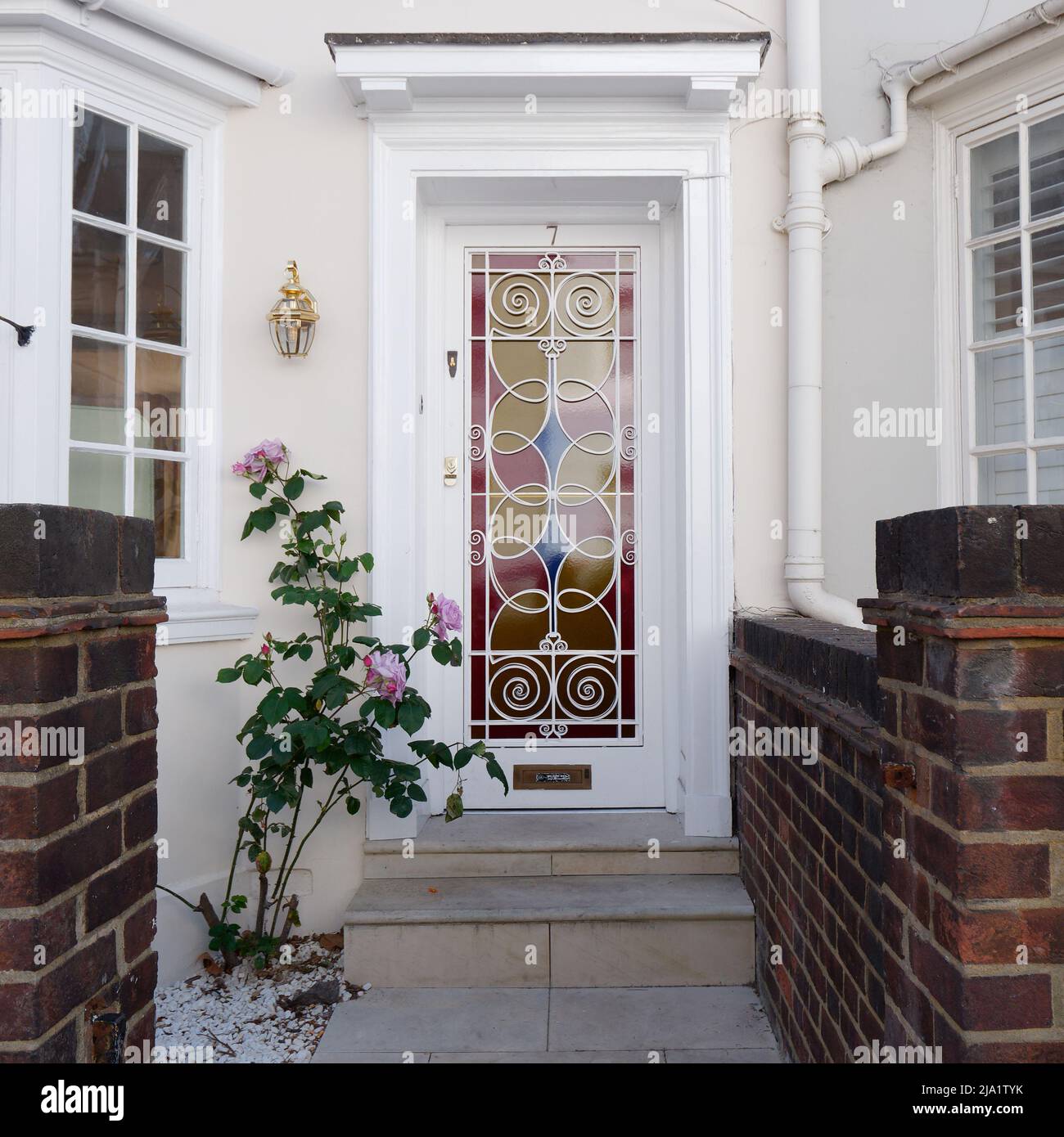 Entrée de la maison avec une porte d'entrée aux vitraux roses, bleus et jaunes et des fleurs roses à l'extérieur, juste à côté de Kings Road à Chelsea, Londres. Banque D'Images