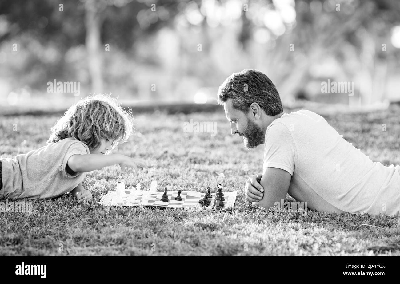 famille heureuse de père et fils enfant jouant aux échecs sur l'herbe verte dans le parc extérieur, fête des pères Banque D'Images