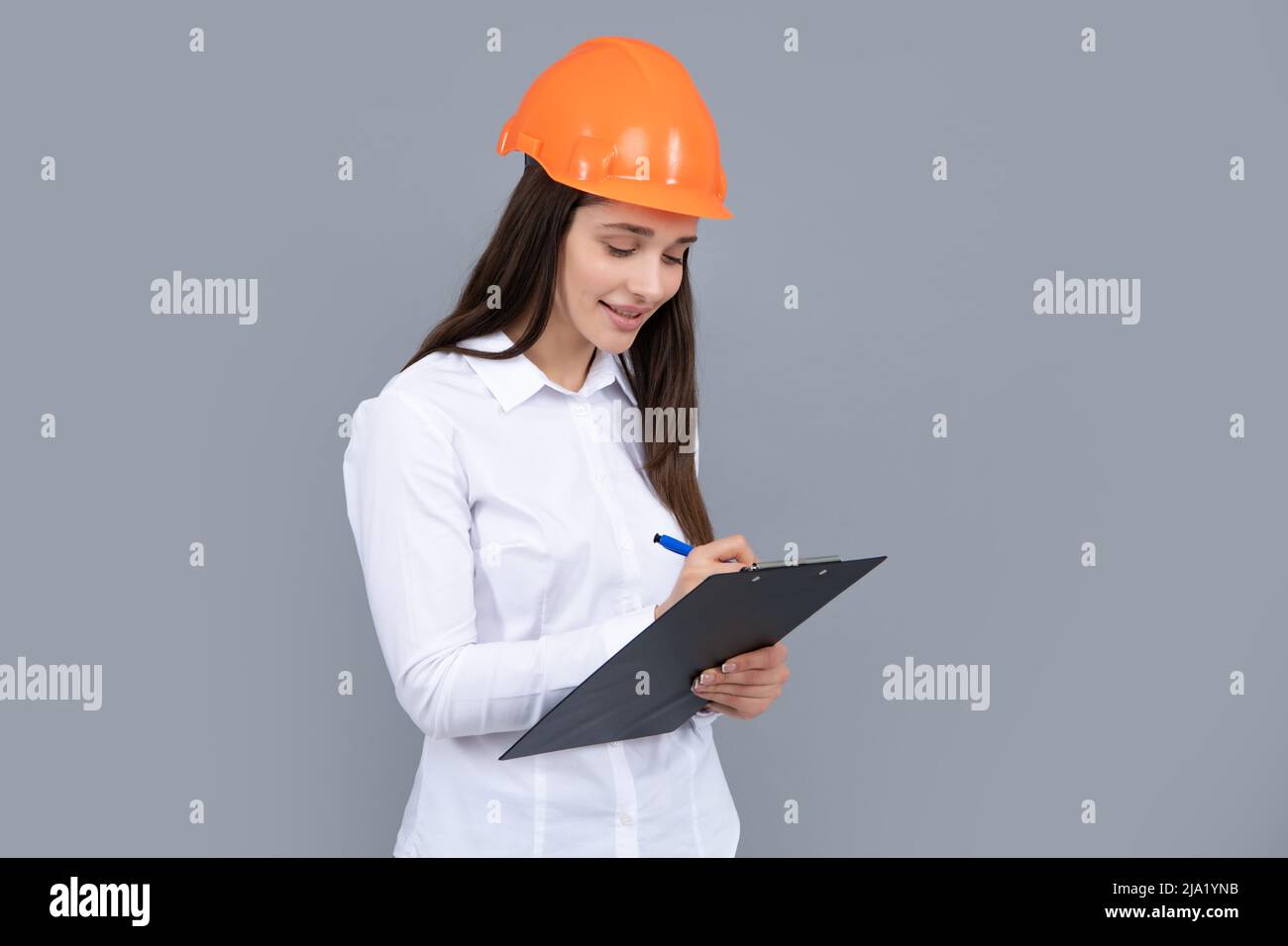 Femme d'affaires avec presse-papiers, portrait sur gris. Portrait d'une femme employée dans un casque de casque. Banque D'Images