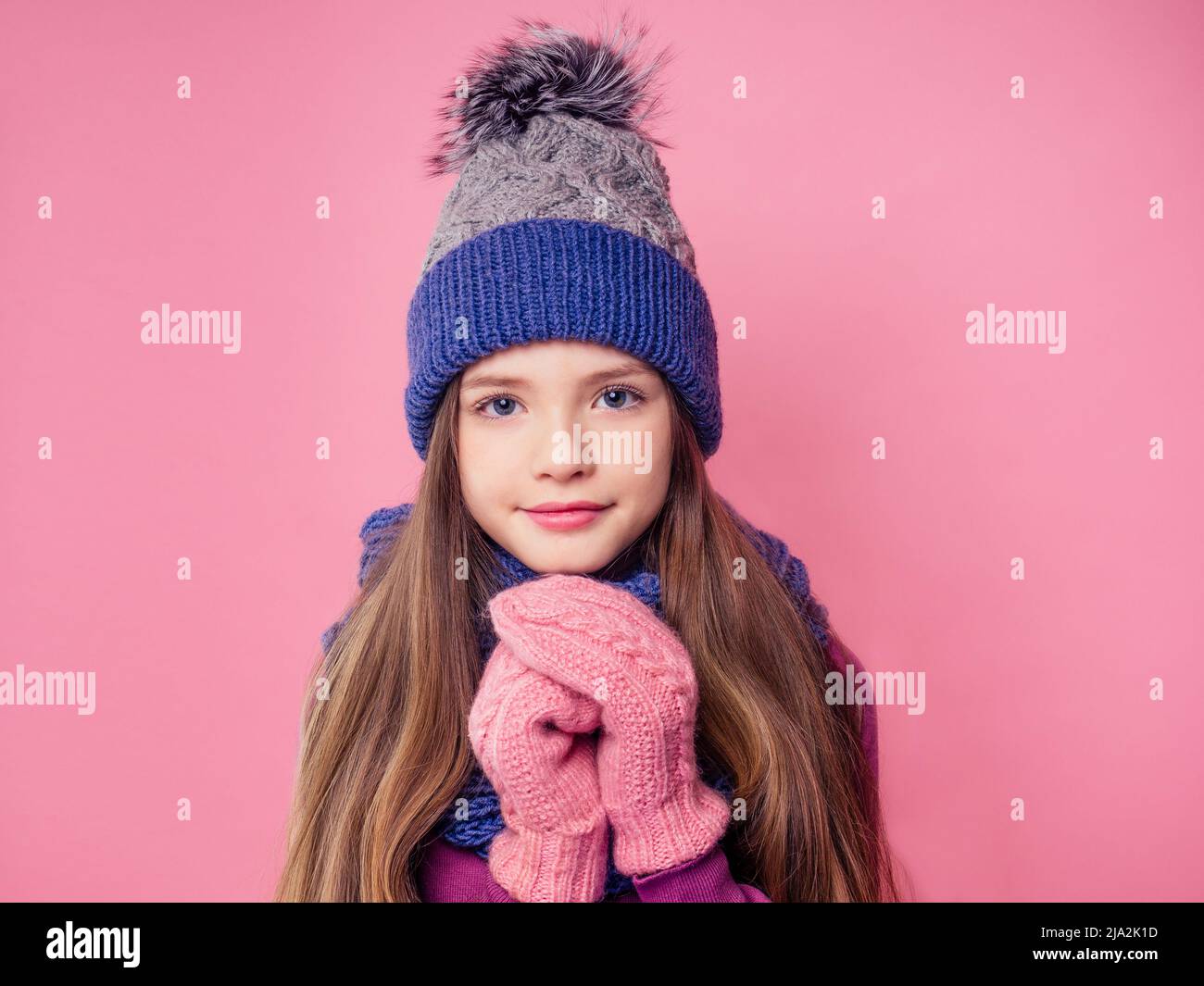 Portrait mignon petite fille en tricoté chaud couleur bleu chapeau, écharpe et mitaines envoi soufflant un air de baiser sur fond rose en studio.enfants Banque D'Images