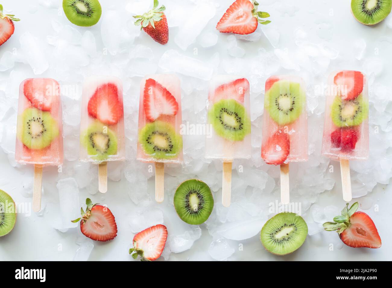 Des papsicles de kiwis aux fraises sur glace entourés de tranches de fraises et de kiwis. Banque D'Images