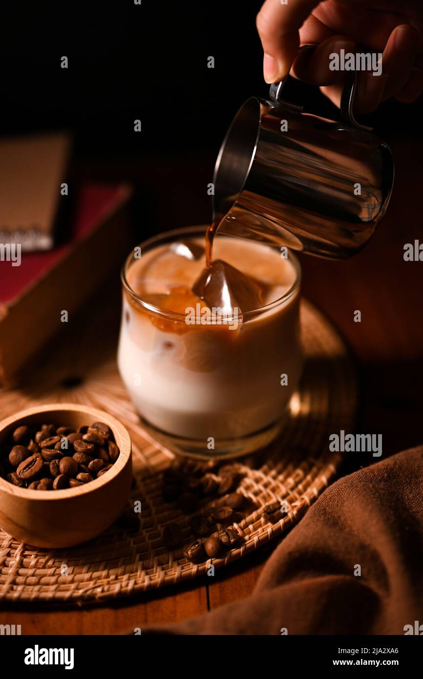Un barista verse un café froid ou un café foncé dans un verre de lait frais. Image du café sur fond sombre. Boissons rafraîchissantes Banque D'Images