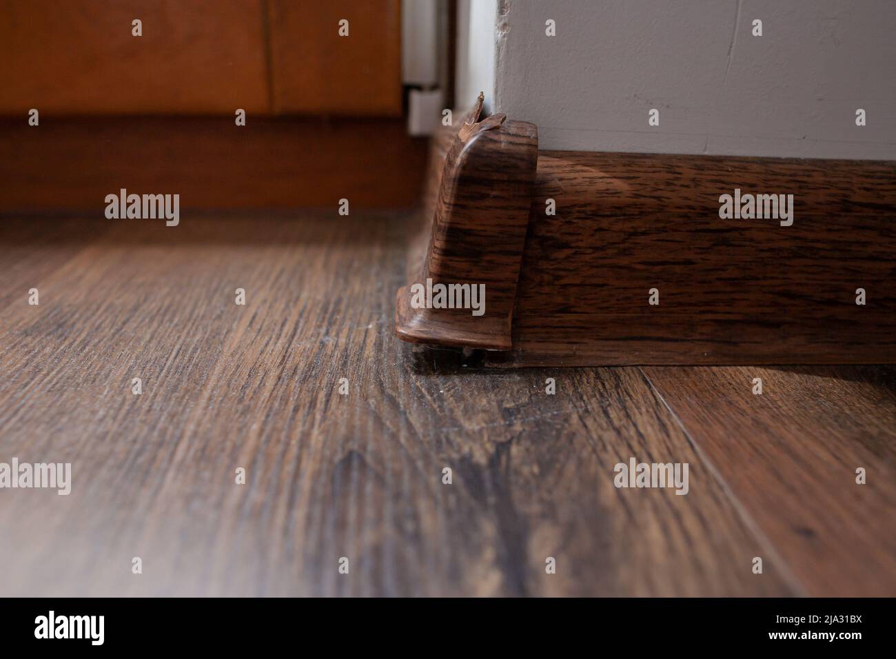 Gros plan d'un coin de plinthe cassé avec fissures, parquet, mur blanc rayé et porte de balcon en bois en arrière-plan Banque D'Images