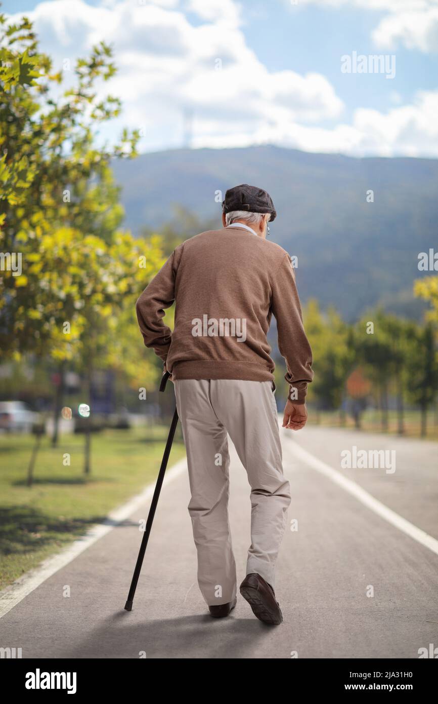 Vue arrière d'un homme âgé marchant avec une canne sur une voie piétonne asphaltée Banque D'Images