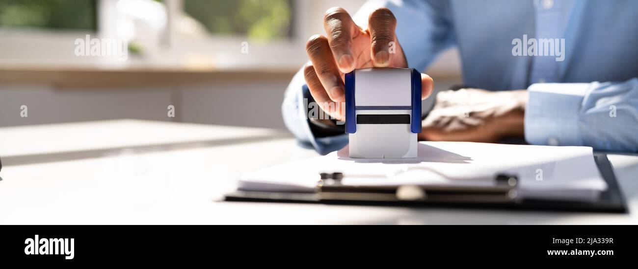 Close-up of a person's Hand Stamping avec timbre approuvé sur le document At Desk Banque D'Images