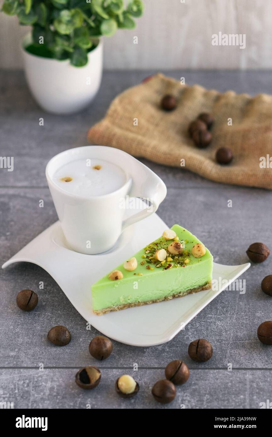 Gâteau au pistache vert avec noix de macadamia sur une assiette blanche et cappuccino. Cheesecake crémeux à la pistache Banque D'Images