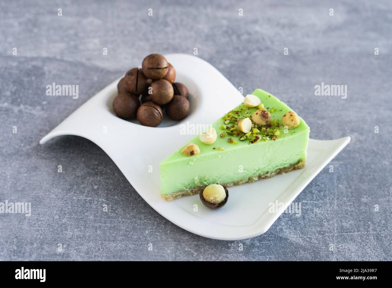 Gâteau vert à la pistache avec noix de macadamia sur plaque blanche sur table en béton gris. Cheesecake crémeux à la pistache Banque D'Images