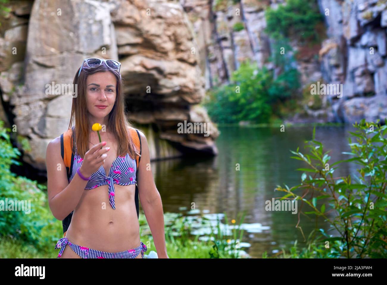 Jolie femme dans un maillot de bain avec une fleur jaune près d'une rivière parmi les rochers sauvages Banque D'Images