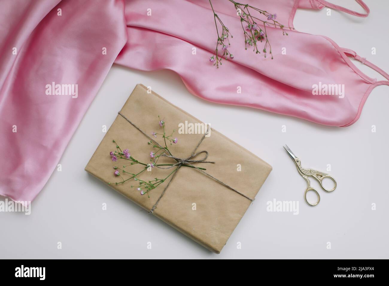 Composition avec tissu en soie rose, cadeau en papier artisanal et fils et ciseaux sur fond blanc. Flat lay, vue de dessus. Concept de loisirs et de loisirs. Banque D'Images