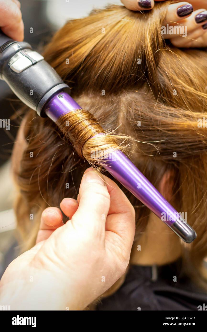 Le coiffeur fait des boucles de cheveux longs bruns avec le fer à friser en  salon de coiffure, gros plan Photo Stock - Alamy