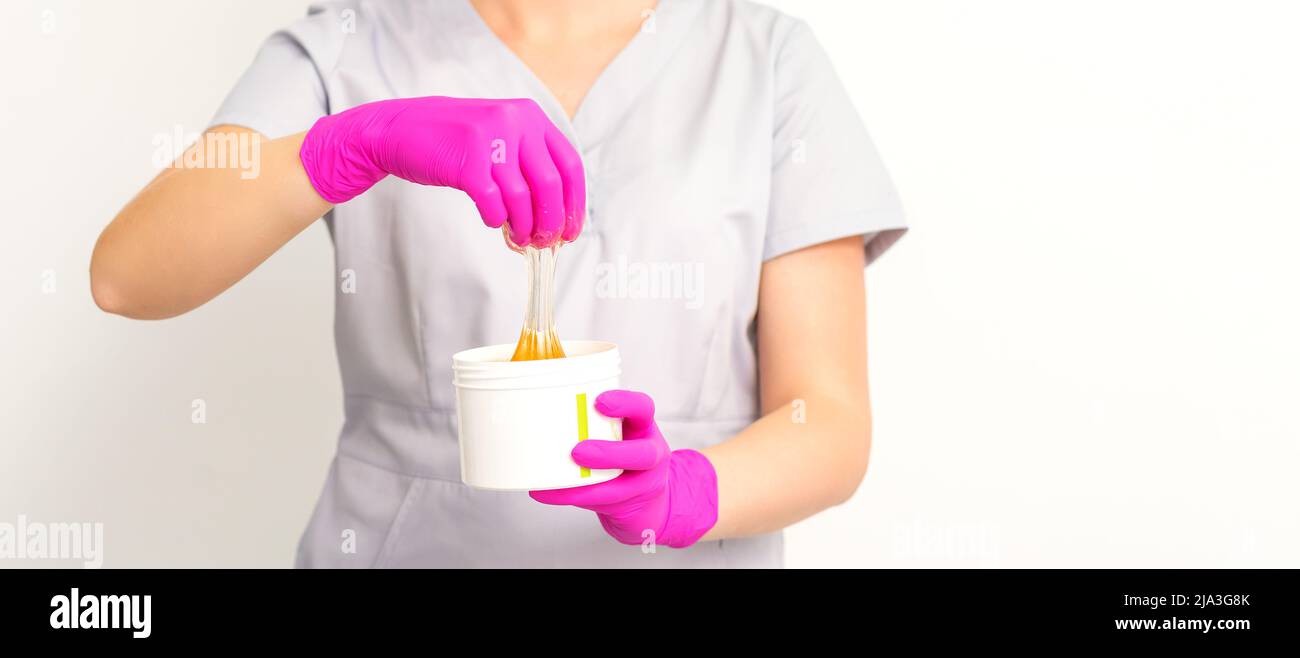 Portrait d'une esthéticienne caucasienne tenant un pot de pâte de sucre pour sugarer portant des gants roses sur fond blanc Banque D'Images