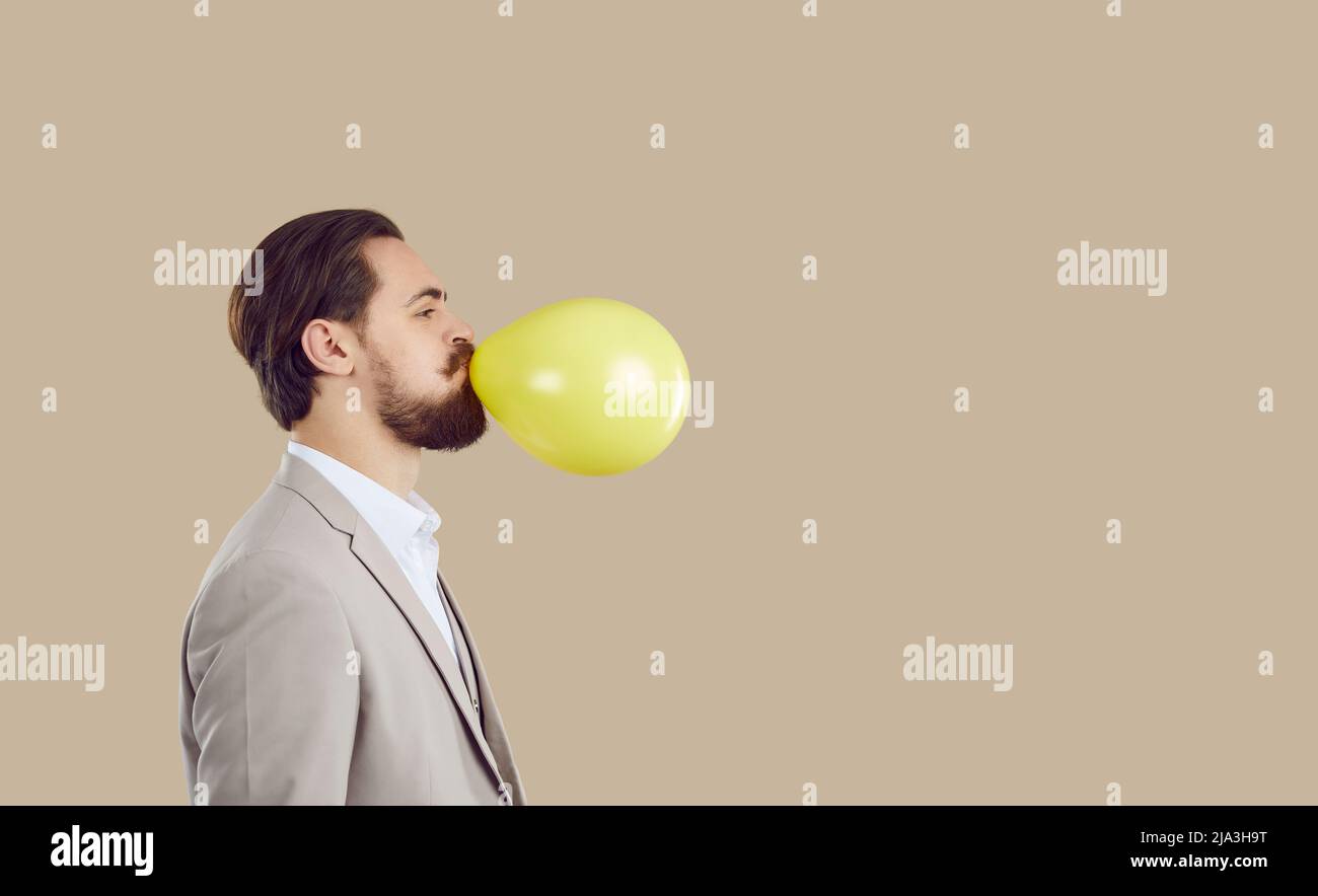 Joyeux homme d'affaires élégant se préparant à la fête en gonflant le ballon gonflable jaune. Banque D'Images