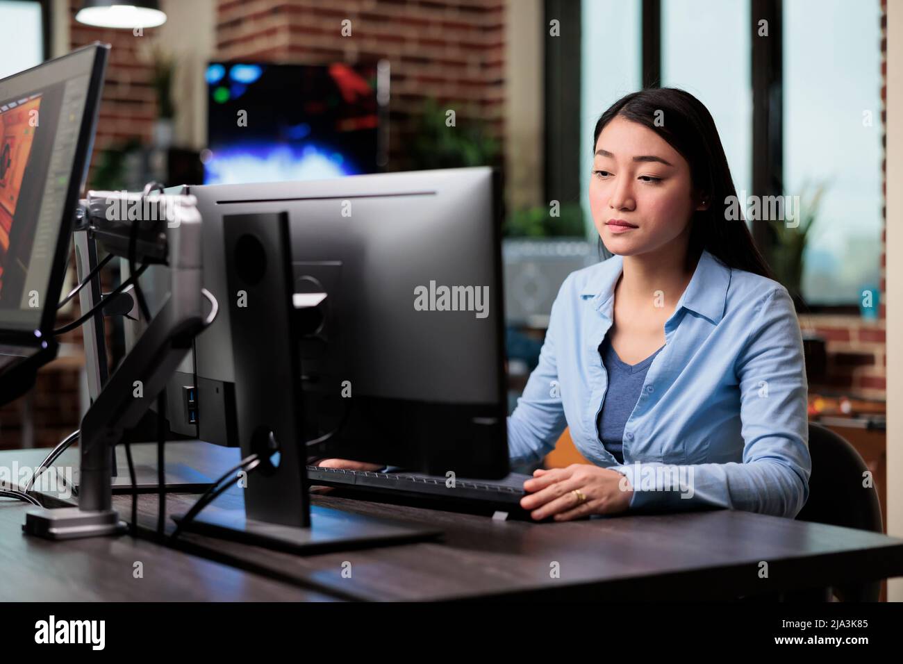 Magnifique artiste créatif asiatique assis à un bureau tout en développant l'art numérique. Employé de bureau de la société dans le département de production travaillant sur l'ordinateur tout en concevant des graphismes modernes. Banque D'Images