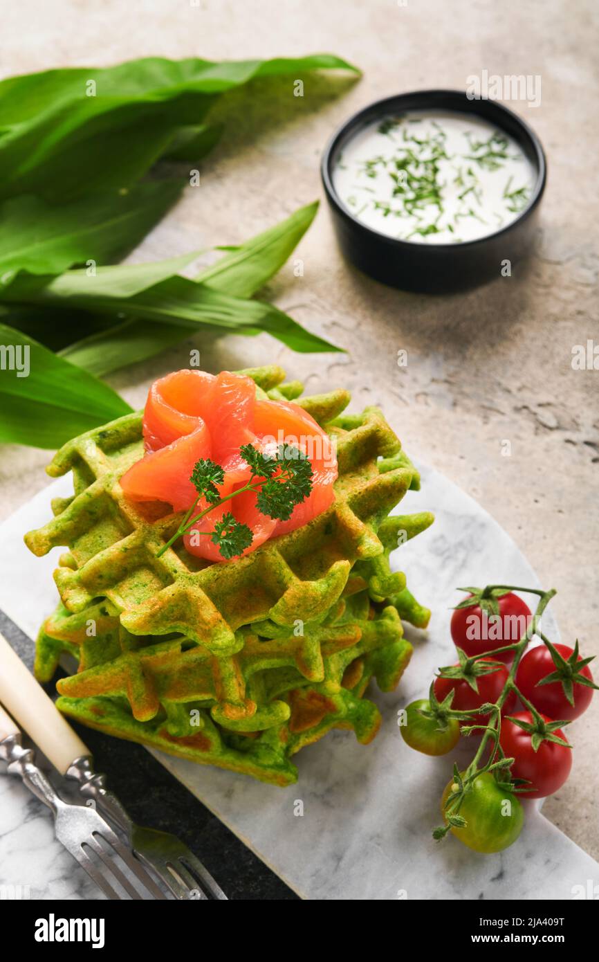 Gaufres belges vertes. Épinards ou ail sauvage ou gaufres au pesto avec saumon rouge et sauce à la crème sur fond de table en béton gris. Délicieux petit déjeuner, Banque D'Images