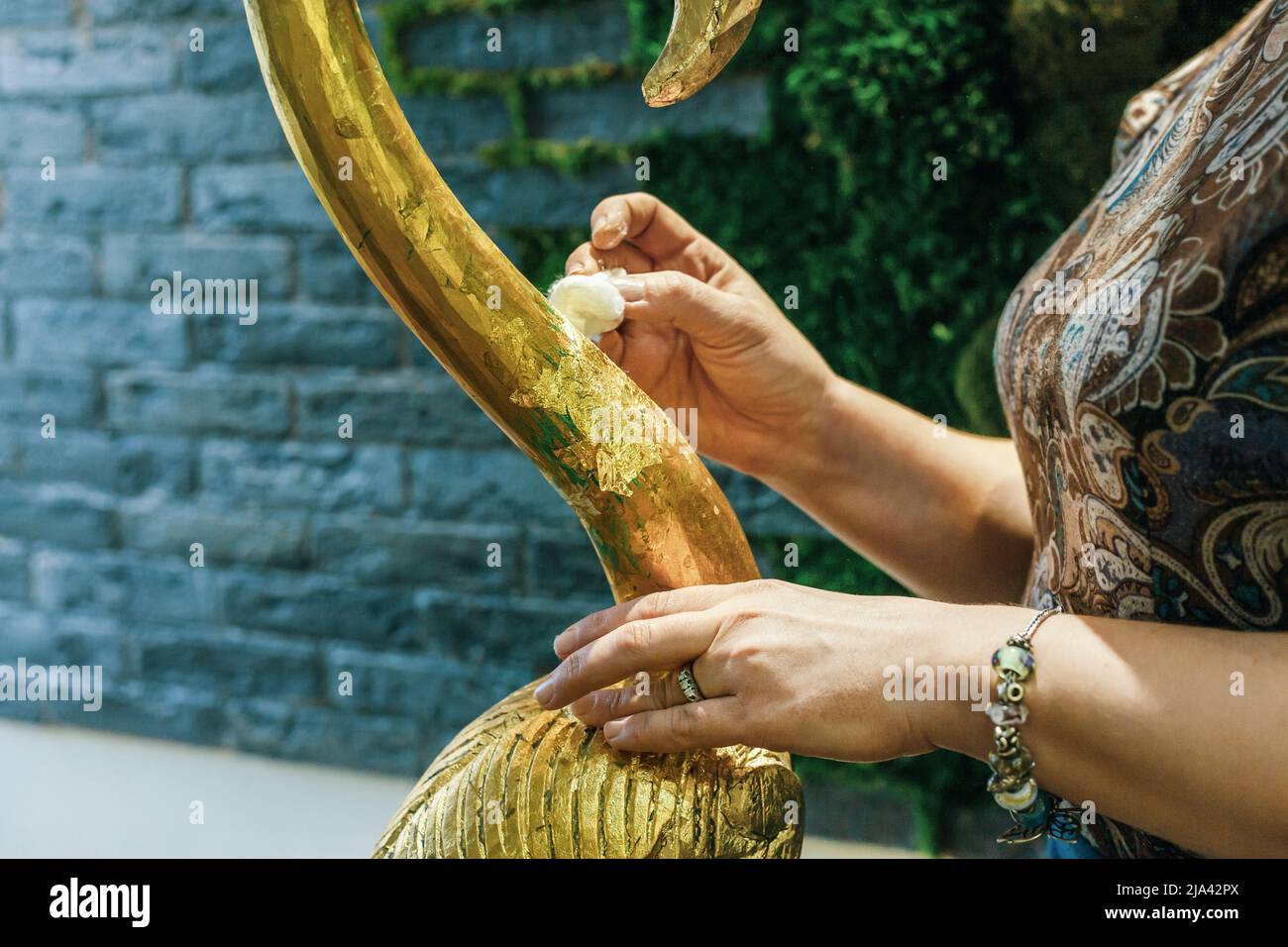 Une femme de créateur restaure et couvre une statuette en bois de flamants roses avec du papier d'aluminium doré. Le processus de dorure manuelle Banque D'Images