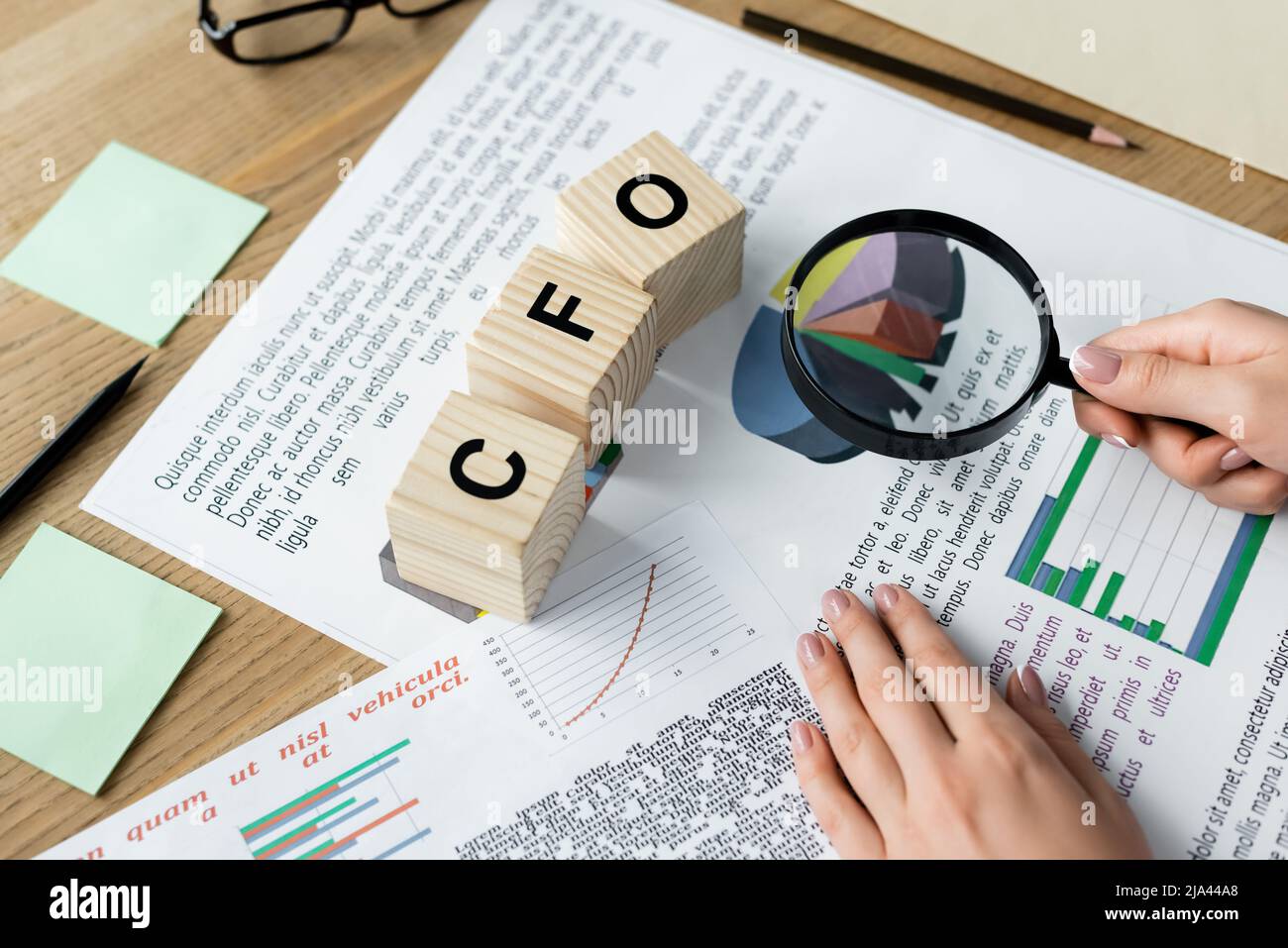 vue rognée de la femme tenant la loupe au-dessus des tableaux près des cubes avec le lettrage cfo sur le bureau Banque D'Images