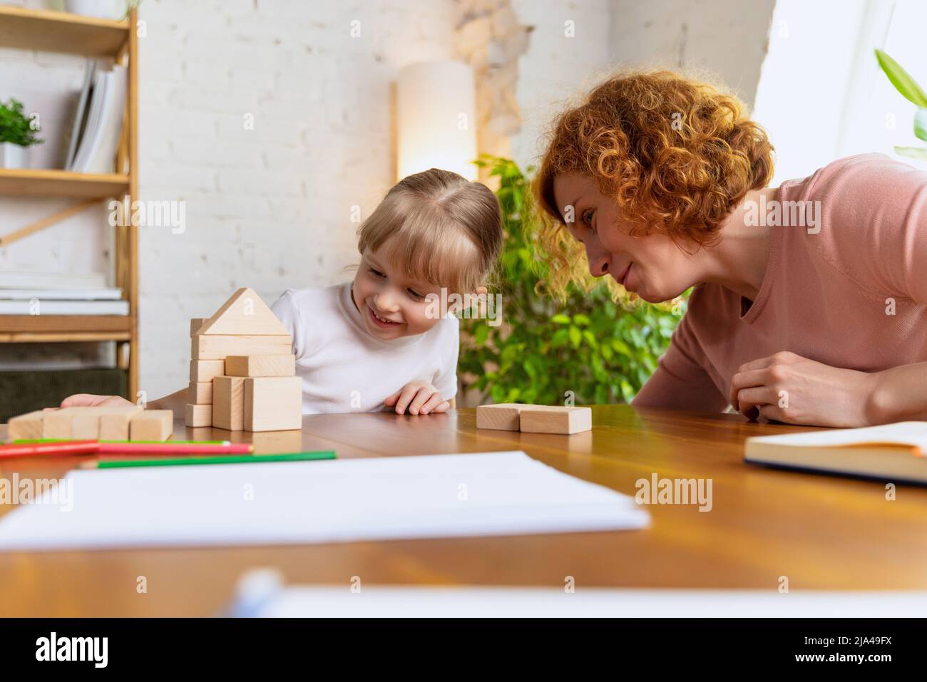 Développer de bonnes aptitudes motrices et la pensée logique. Femme souriante et petite fille mignonne, mère et fille jouant avec des cubes de jouet en bois à la maison. Concept Banque D'Images