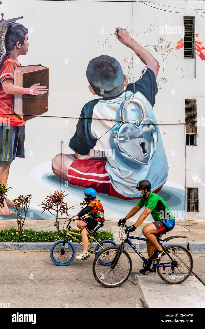 Deux cyclistes passant par Une fresque murale colorée dans le district de Barranco, Lima, Pérou. Banque D'Images
