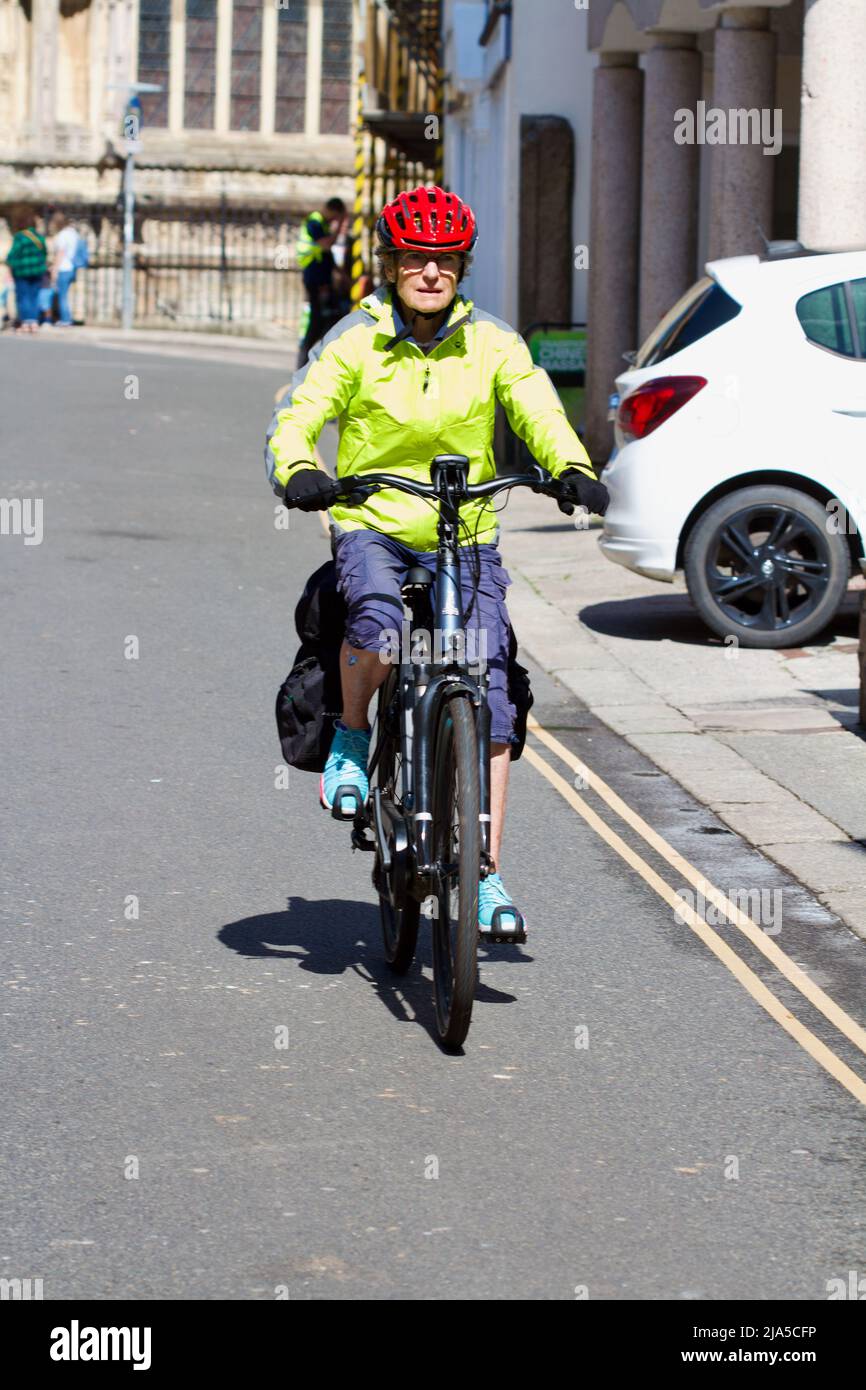 Une femme qui roule à vélo électrique vers vous tout en portant une veste de vélo fluorescente et un casque rouge Banque D'Images