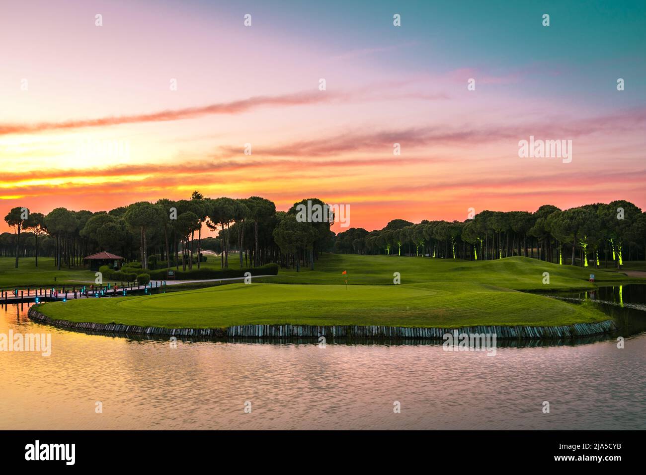 Vue panoramique sur le magnifique parcours de golf avec pins au coucher du soleil. Terrain de golf avec fairway, lac et pins Banque D'Images