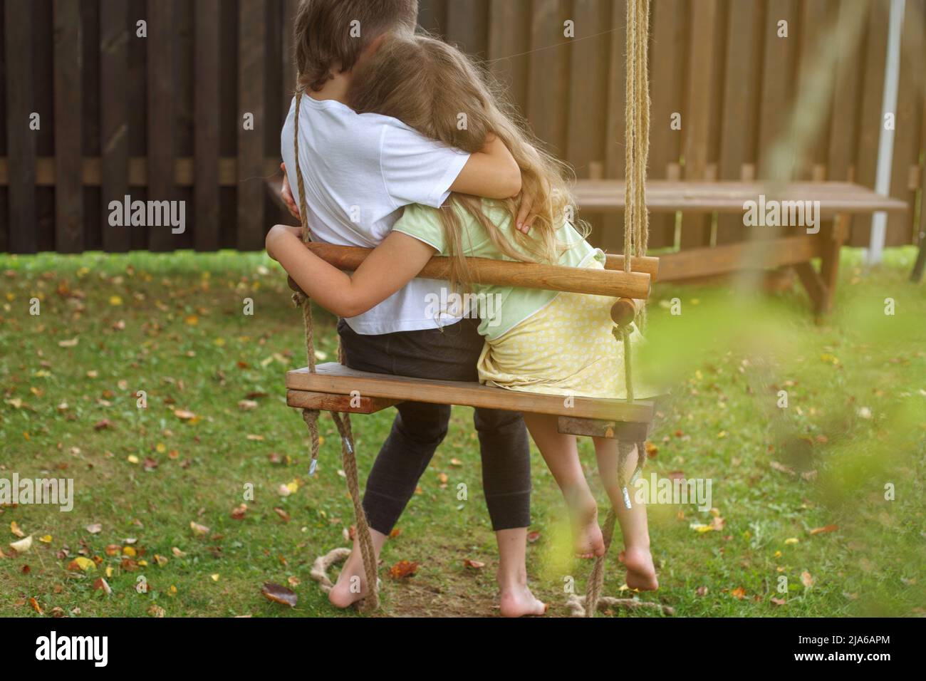 enfants assis sur une balançoire dans le jardin. frère aîné embrassant la petite sœur. Banque D'Images