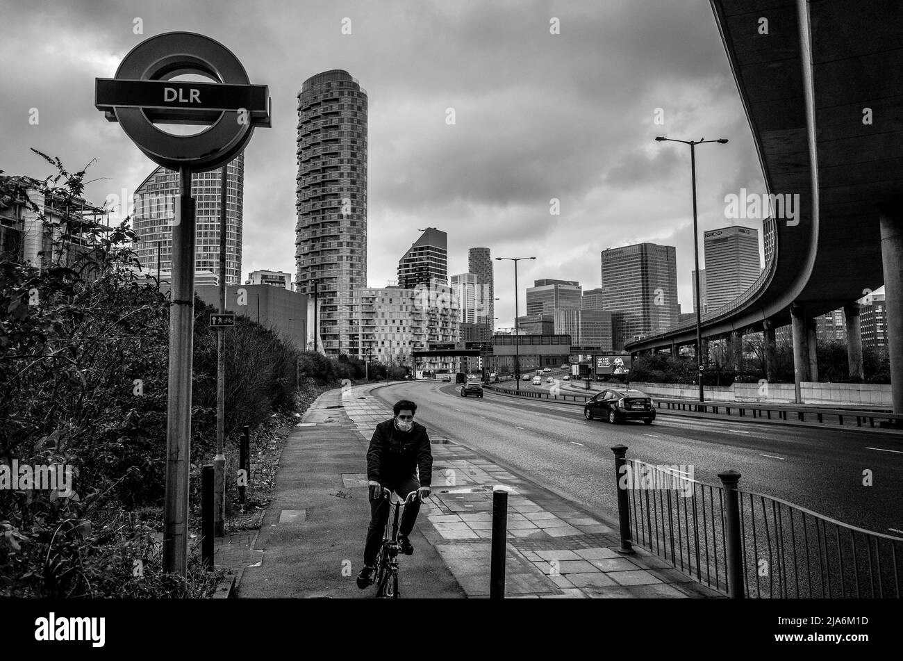 Le paysage urbain de l'est de Londres, un cycliste passe tout en marchant le long de West India Dock Road vers l'île des chiens. Banque D'Images