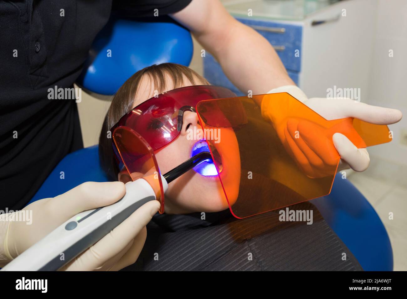 La petite fille reçoit un traitement médical de l'stomatologiste, faisant la procédure avec la lumière UV de cure dentaire en clinique Banque D'Images