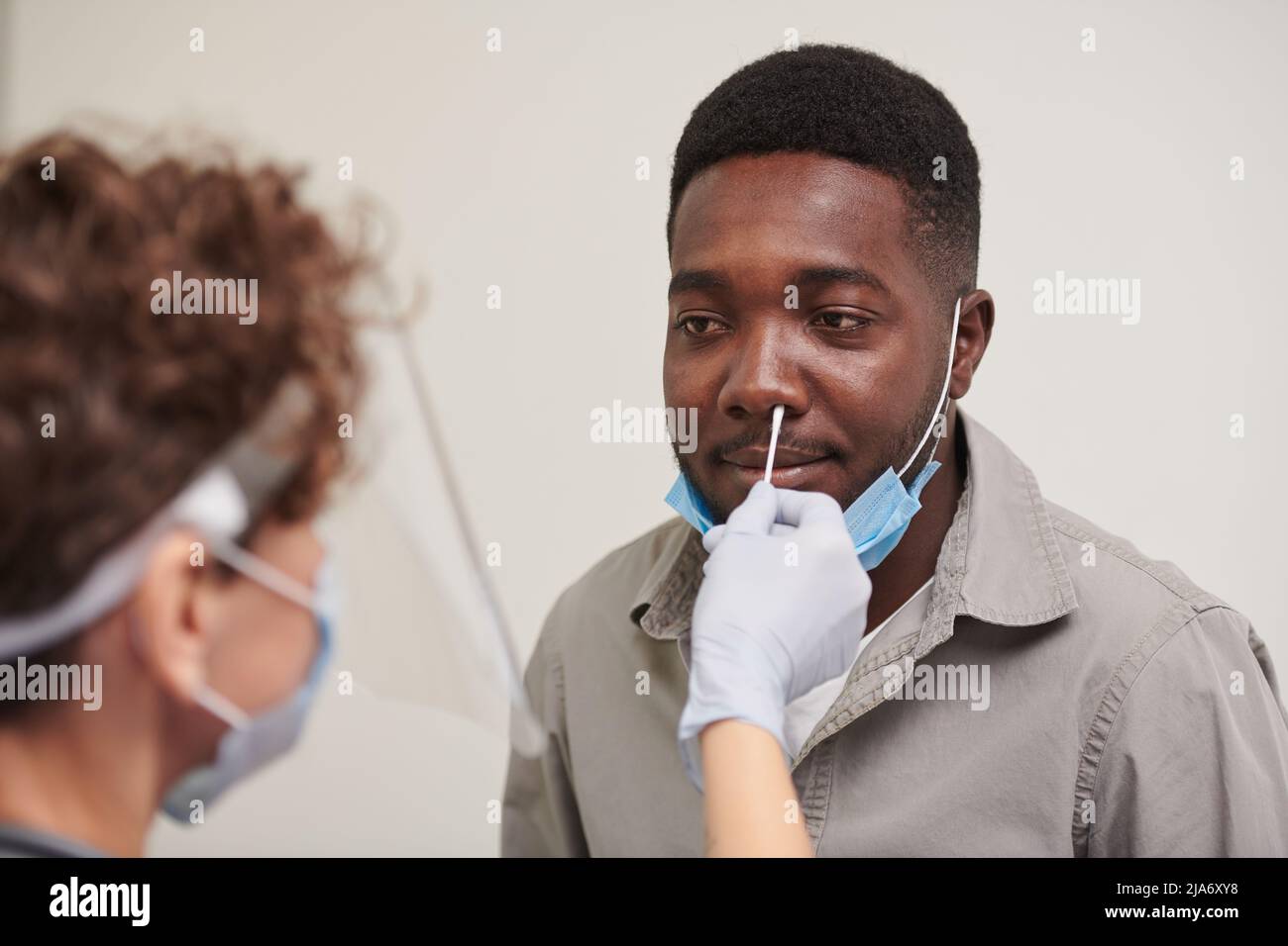 Gros plan moyen à grand angle d'un médecin méconnaissable portant un masque de protection qui teste la présence d'une maladie virale chez un homme afro-américain Banque D'Images