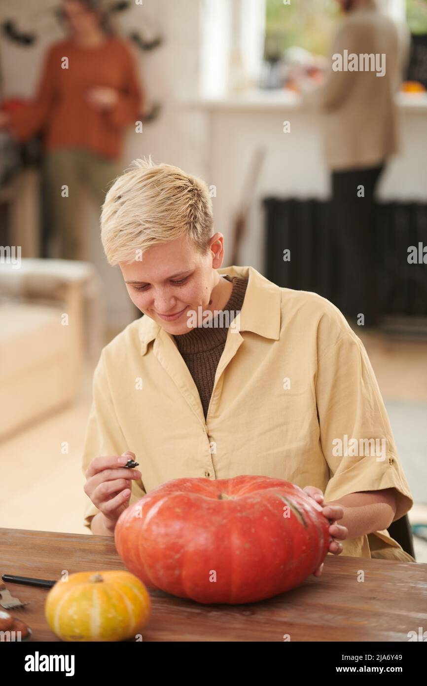 Jeune femme souriante aux cheveux blonds assis à la table et créant le motif sur la citrouille d'Halloween Banque D'Images