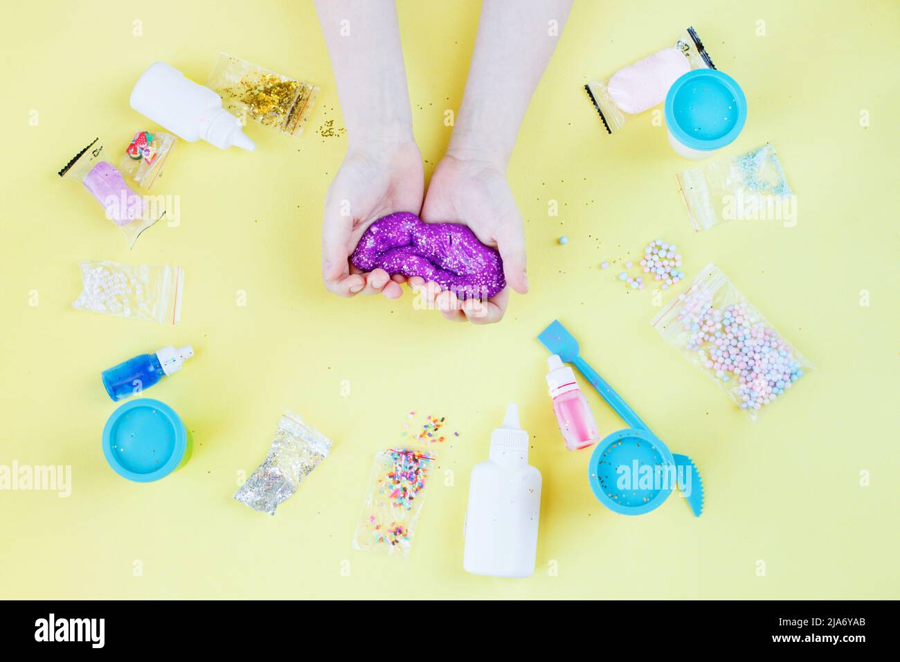 Faire de la chaux à la maison. Enfant tenant et étirant de la chaux colorée. DIY concept.Kids Hands font de la chaux violette avec des paillettes sur un fond jaune. Plat Banque D'Images