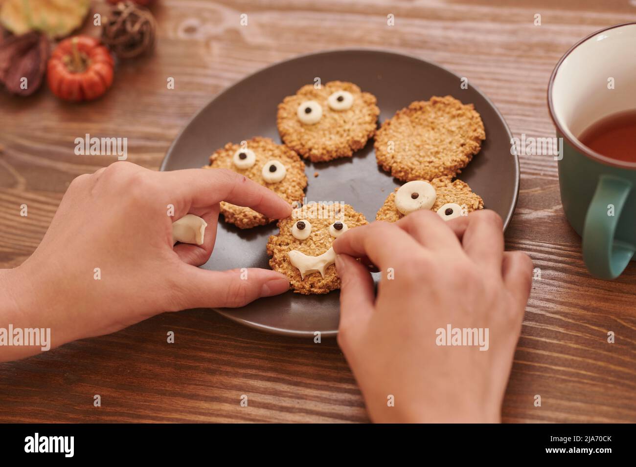 Les mains faisant le visage givrant sur les biscuits de sucre placés sur l'assiette, préparant des bonbons pour Halloween Banque D'Images