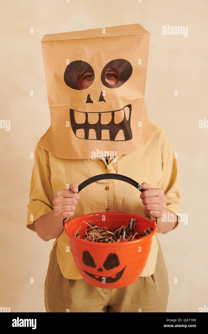 Portrait d'une femme dans un sac en papier avec grimace souriant, se tenant debout sur un arrière-plan isolé et donnant des gâteries pour Halloween Banque D'Images