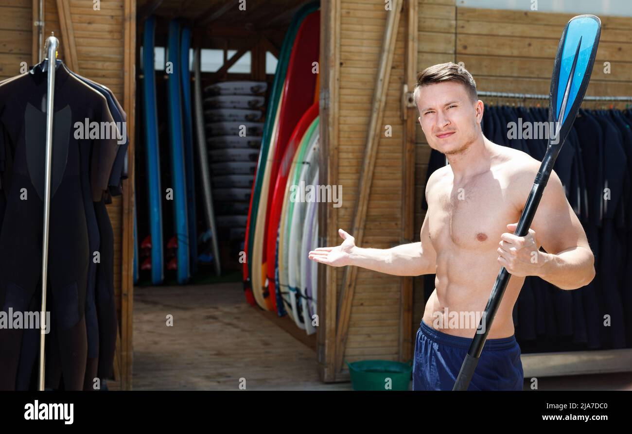 Entraîneur de surf de type sportif attendant les clients à côté des casiers avec l'équipement dans le club de plage Banque D'Images