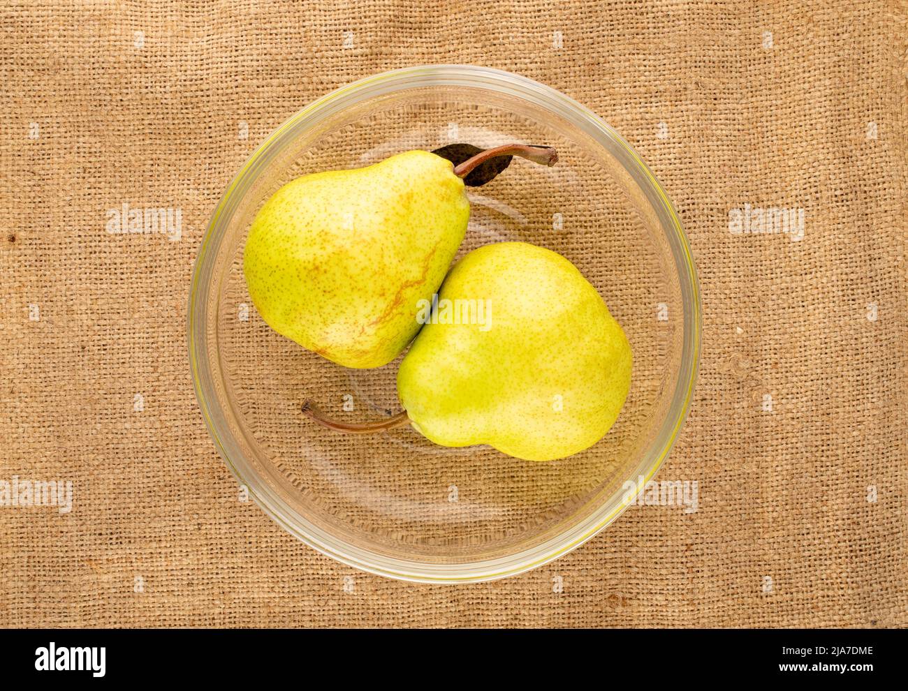 Deux poires biologiques juteuses dans un bol en verre sur un chiffon jute, vue rapprochée du dessus. Banque D'Images