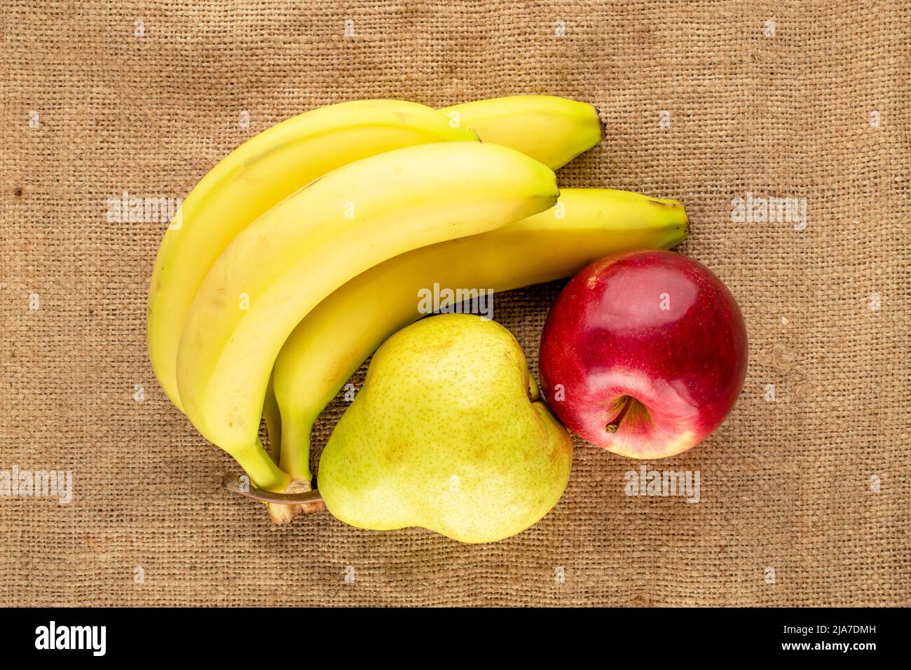 Une poire biologique juteuse, pomme rouge et bouquet de bananes sur du jute, vue rapprochée, vue du dessus. Banque D'Images