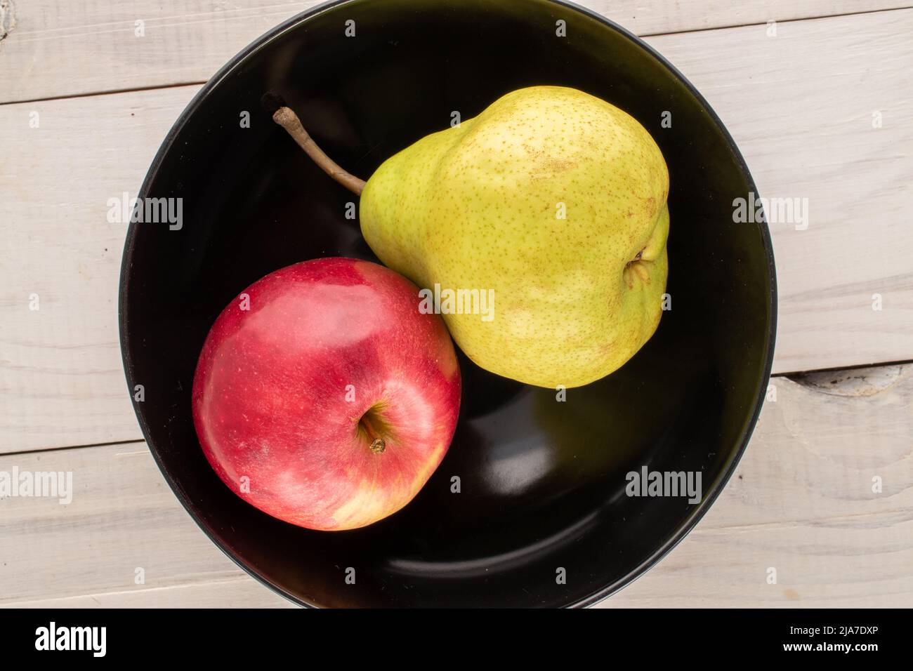 Une poire biologique juteuse et une pomme rouge dans une plaque en céramique noire sur une table en bois, vue rapprochée, vue de dessus. Banque D'Images