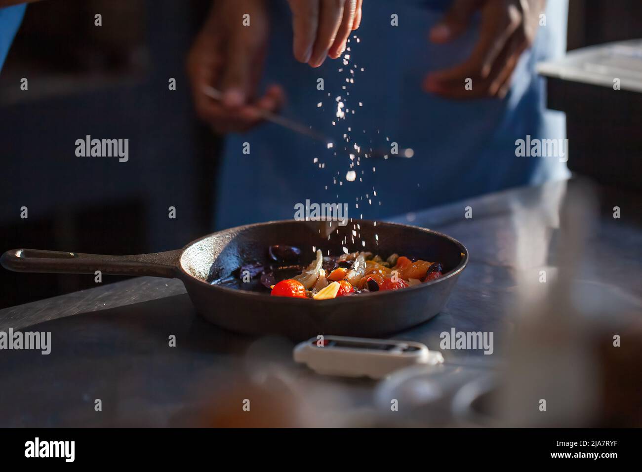 Le chef cuisinier prépare des légumes dans un restaurant de luxe ou dans la cuisine de l'hôtel. Les mains de l'homme ajoutent le sel dans les légumes rôtis dans la casserole. Cuisinier professionnel en uniforme Banque D'Images