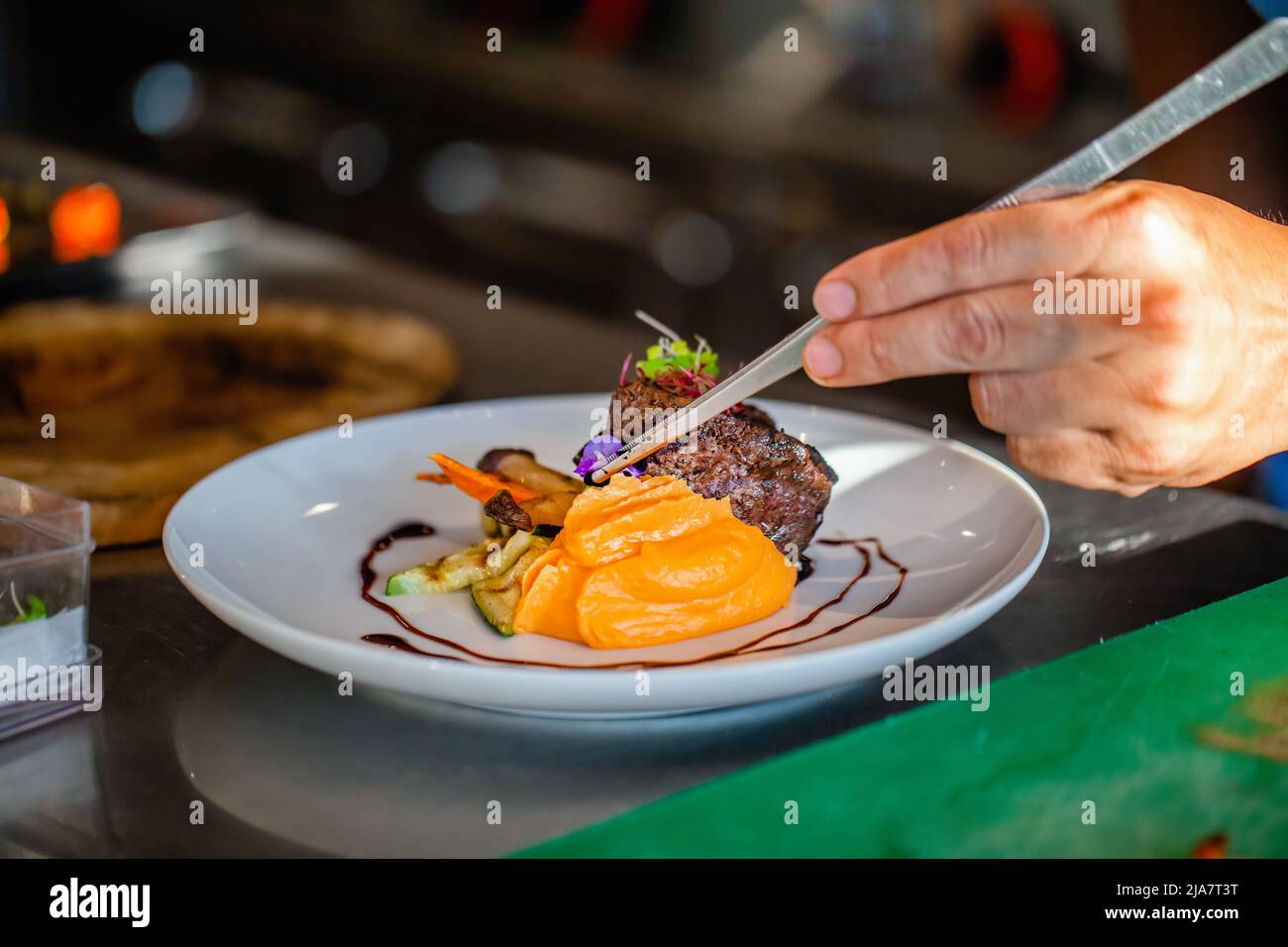 Gros plan des mains du chef dans la cuisine de l'hôtel ou du restaurant décorant le plat. Préparer le steak de bœuf avec la purée de pommes de terre, ajouter les légumes, décorer le plat avec Banque D'Images