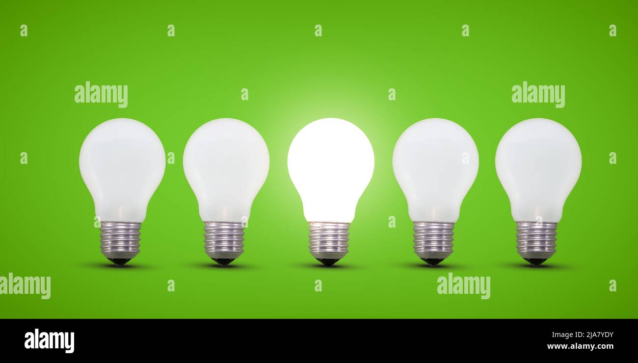 Cinq ampoules d'éclairage dans une rangée, l'ampoule de feu central est très éclairée. Arrière-plan vert. Concept d'idée. Banque D'Images