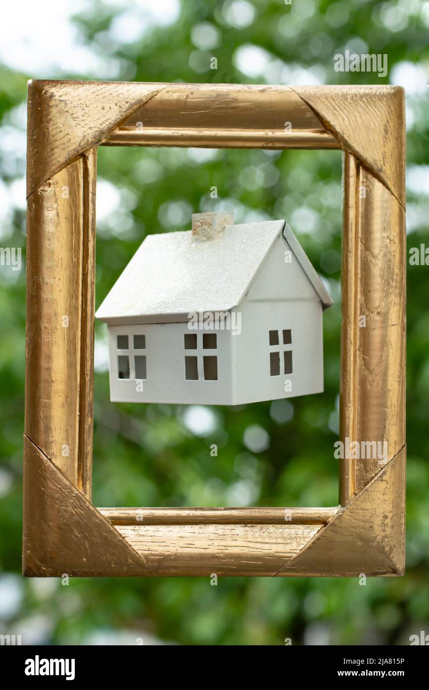 Maison blanche miniature lévitant à l'intérieur d'un cadre doré, sur fond de feuillage vert Banque D'Images