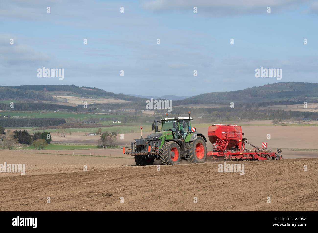 Un paysage agricole pittoresque à Aberdeenshire, avec un tracteur et un semoir fonctionnant dans un champ labouré et une vue sur les terres agricoles au-delà Banque D'Images