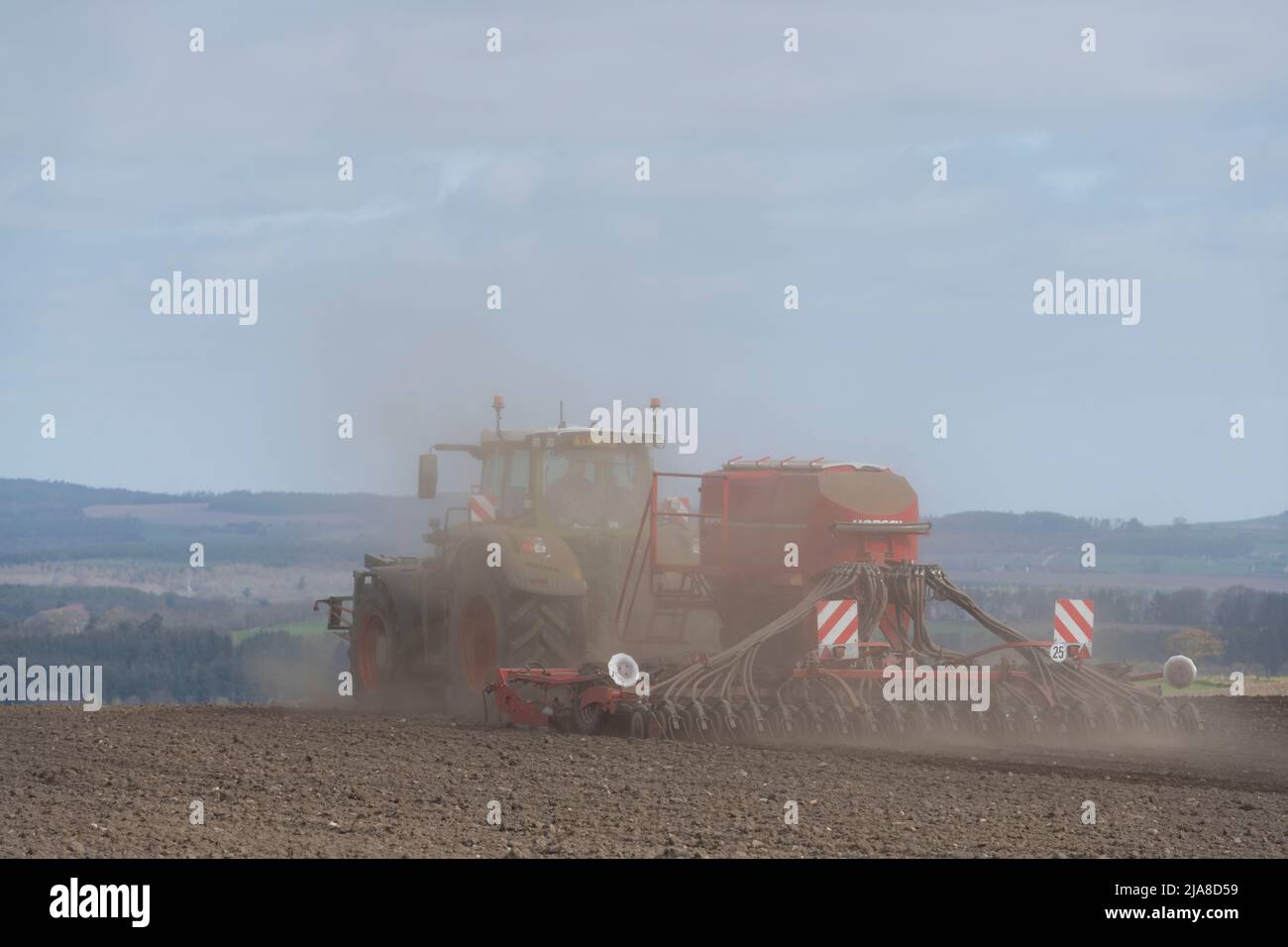 Des nuages de poussière s'élèvent derrière une perceuse à disque Red Horsch remorquée par un tracteur Fendt dans un champ labouré sec sur une ferme écossaise Banque D'Images