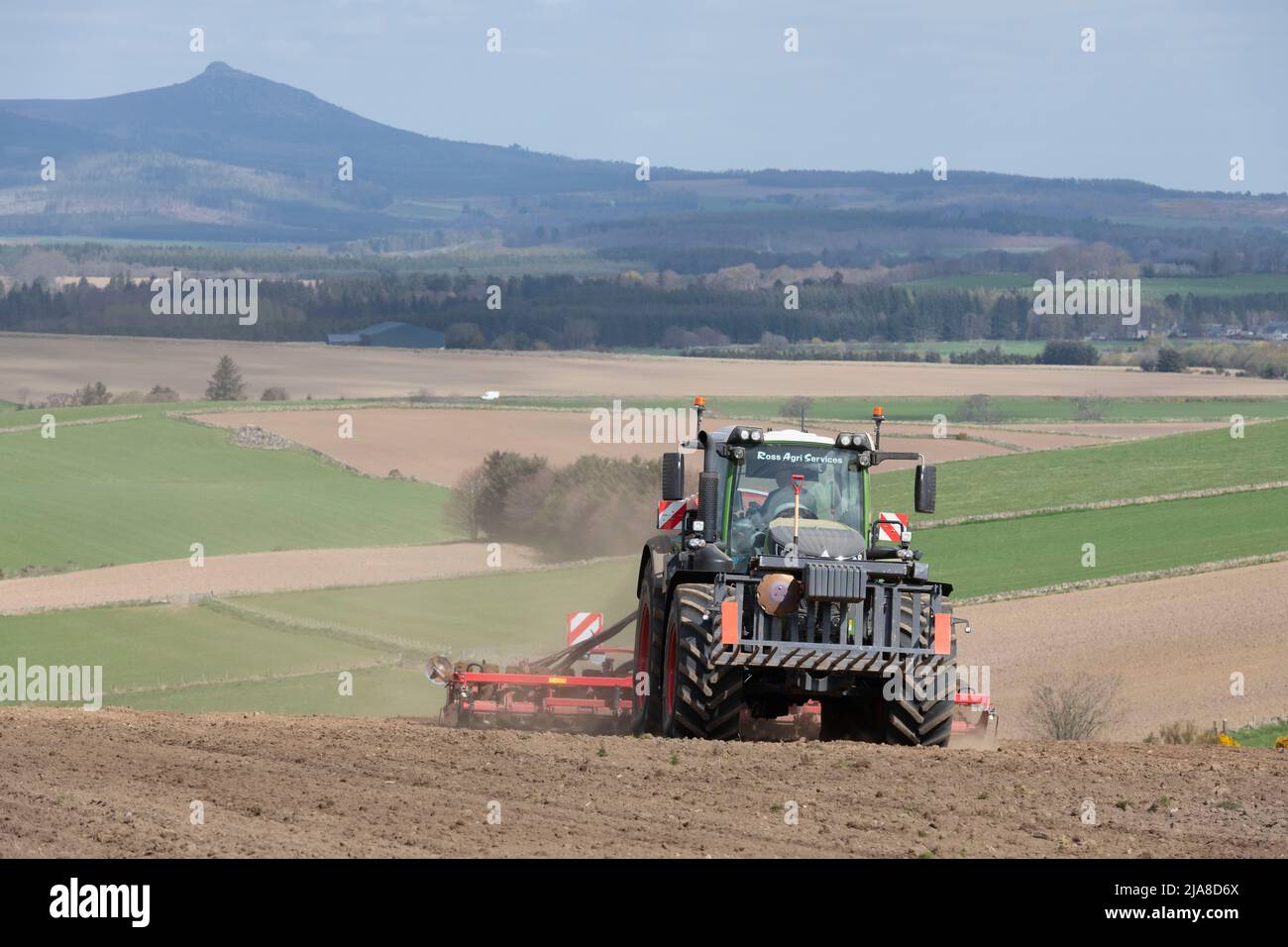 Un tracteur vert Fendt et un semoir universel semis d'orge lors d'une journée ensoleillée dans une ferme d'Aberdeenshire avec Bennachie au loin Banque D'Images