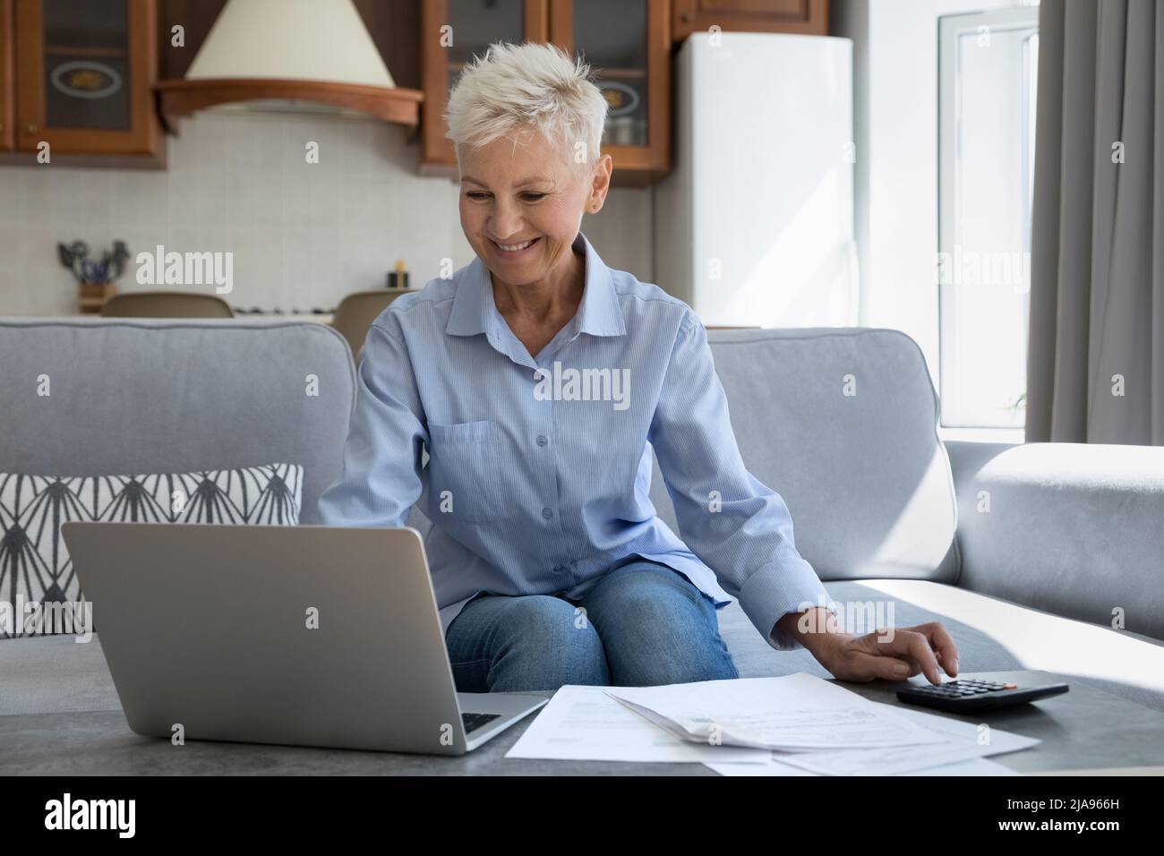 Grand-mère mûr et souriant assis sur un canapé engagé dans la paperasserie Banque D'Images