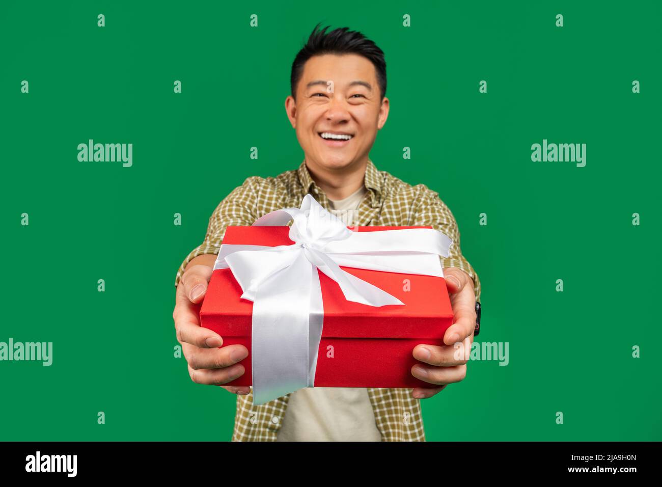 Surprise de vacances. Joyeux homme asiatique d'âge moyen donnant une boîte cadeau à l'appareil photo et souriant, fond vert de studio Banque D'Images