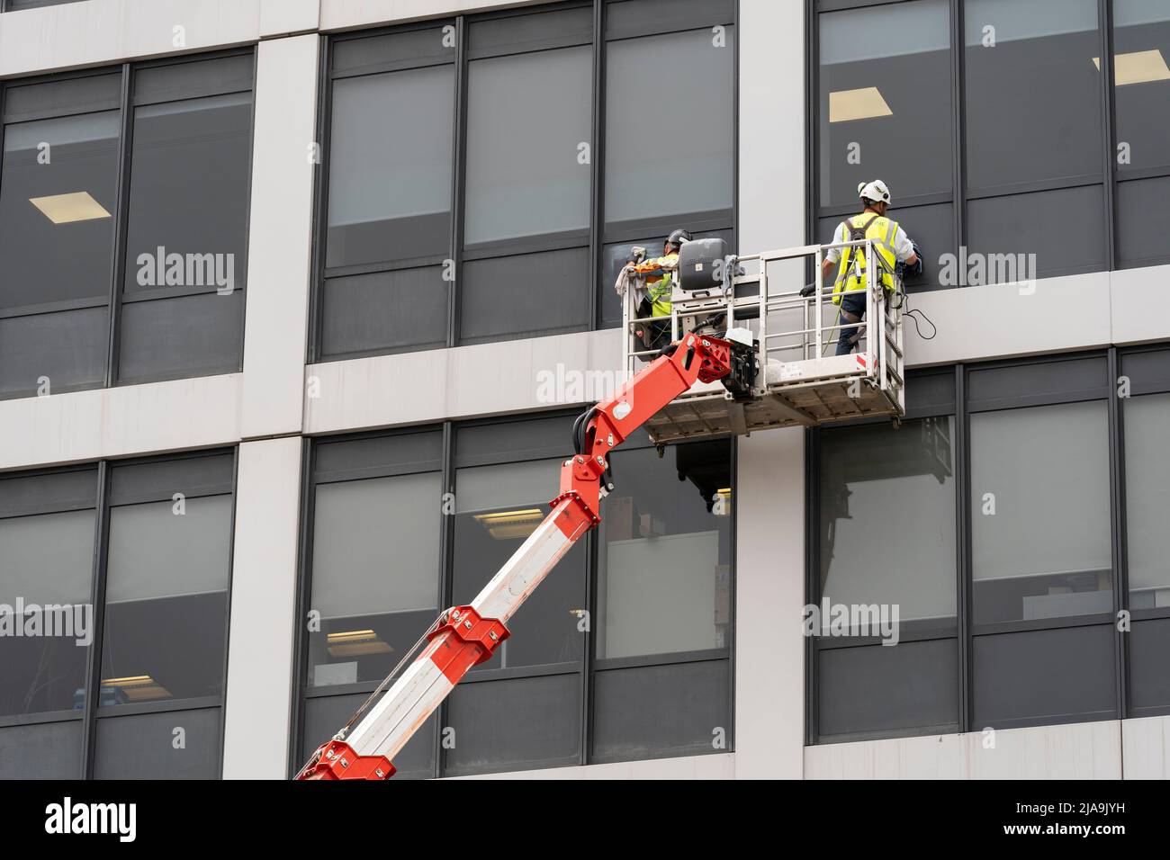 Des hommes travaillant sur une plate-forme de travail mobile surélevée (MEWP) portant des EPI personnels et nettoyant les fenêtres d'un bureau à plusieurs étages de Basingstoke. Angleterre Banque D'Images