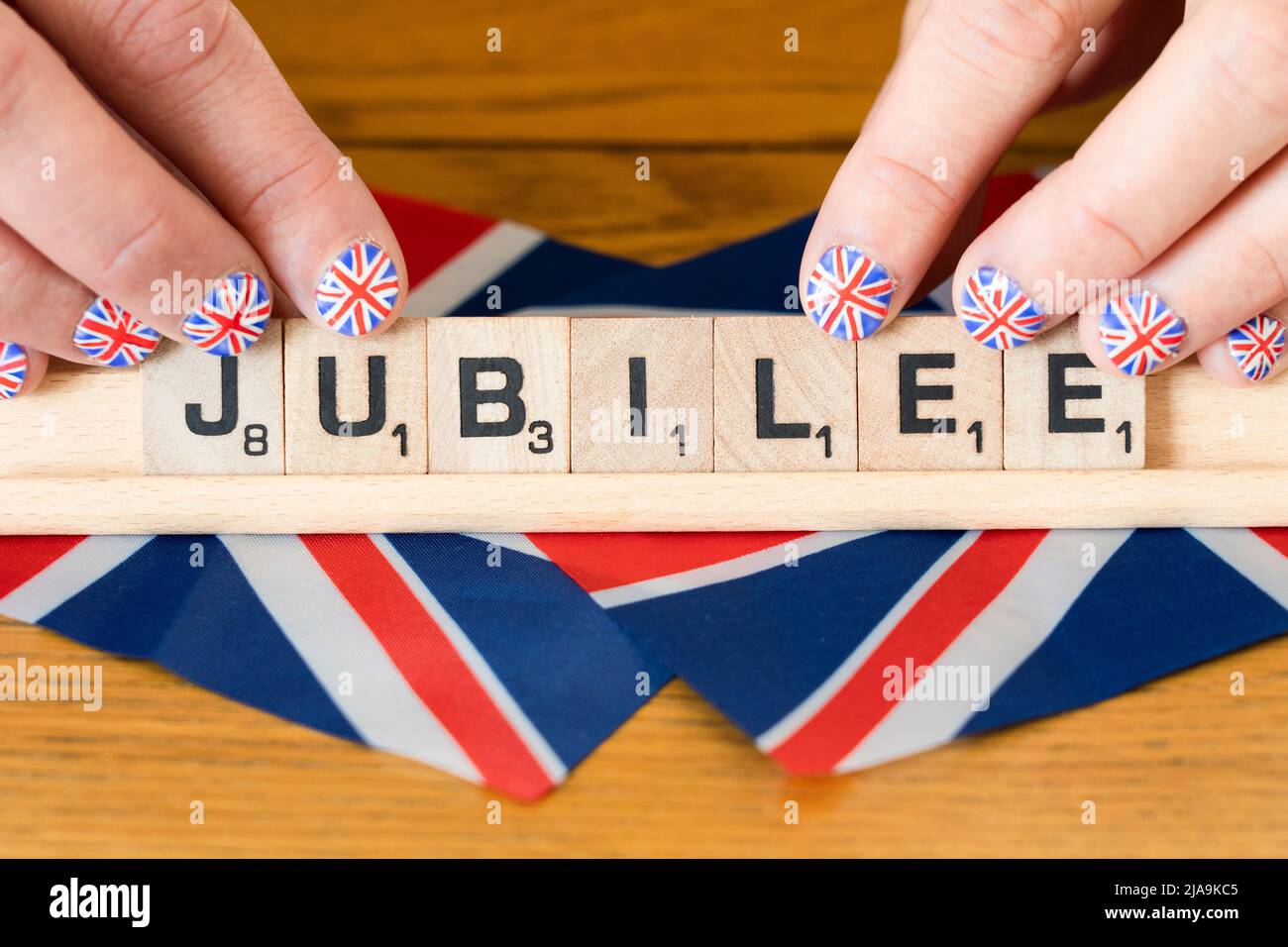 Doigts de femme avec ongles peints avec le drapeau britannique tenant des lettres scrabble qui sort Jubilé - le jubilé de platine de la Reine juin 2022 Banque D'Images