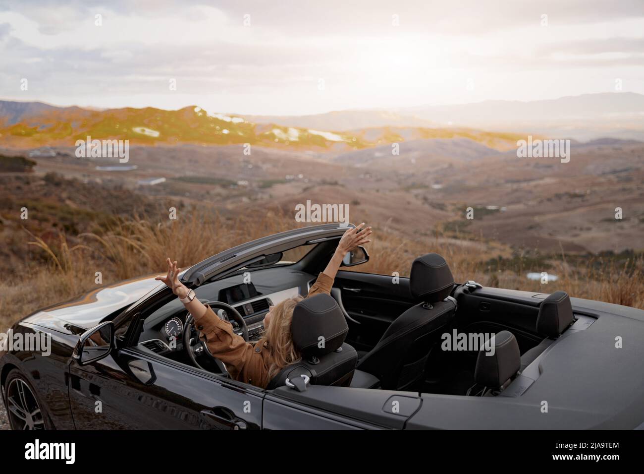 Arrière d'une jeune femme plutôt heureuse tenant la main vers le haut se sentant libre assis dans une voiture convertible Banque D'Images