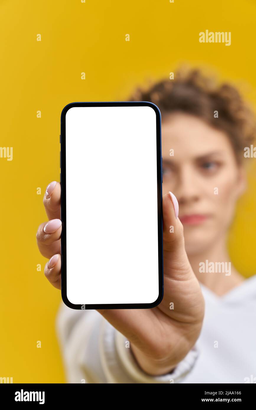 Grave fille floue montrant allumé à l'écran téléphone en studio. Vue rognée d'un smartphone de poche féminin avec écran blanc vierge, isolé sur fond orange, espace de copie. Concept de gadget. Banque D'Images